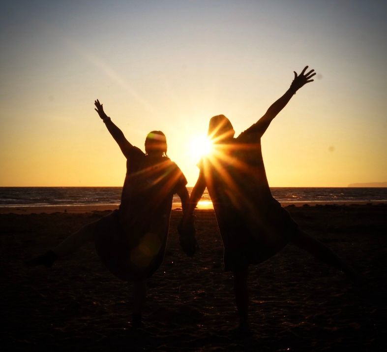 2 friends silhouetted by the sunrise in front of the sea
