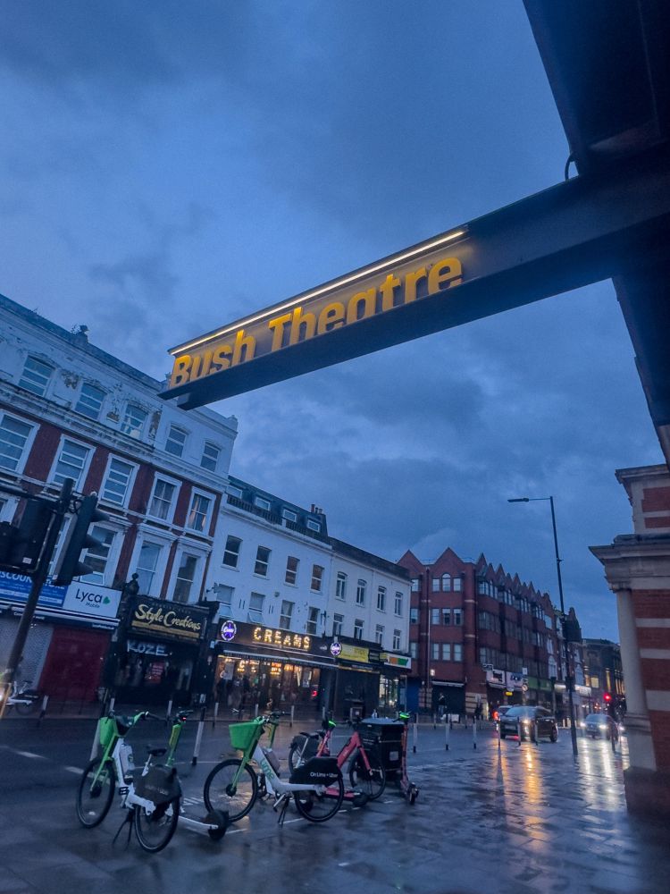 Buildings and Lime bikes and bush theatre sign and cats with headlights in background  