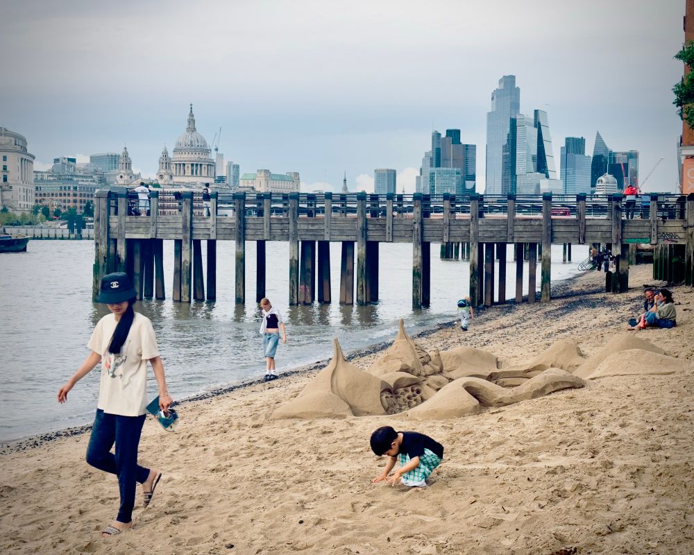 London ‘beach’ including sandcastle sculpture flood preventer people and cityscape in background including gherkin and St Paul’s 