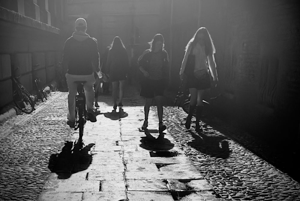 4 people on street one on a bike and their shadows 