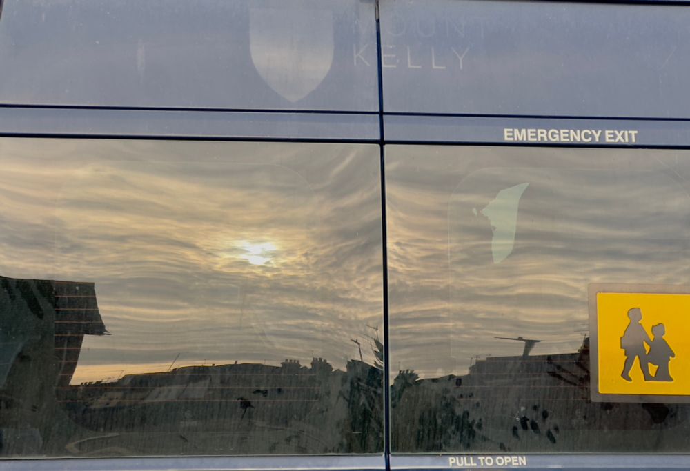 Clouds and sun in back of school minibus with yellow children crossing sign