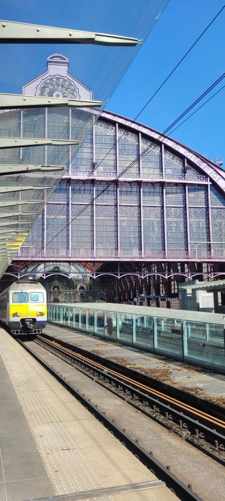 View from the traintracks to the trainstation. We see one train and the sky is blue.