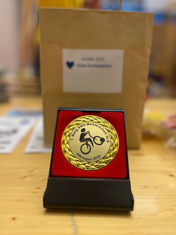 Bild der goldenen Sieger Medallie mit dem Text "1. Rang NWS-Meisterschaft NLB" auf der oberen Seite der Medallie, in der Mitte ist ein Piktogram eines Radball Spielers und unten steht "Oftringen 2025"