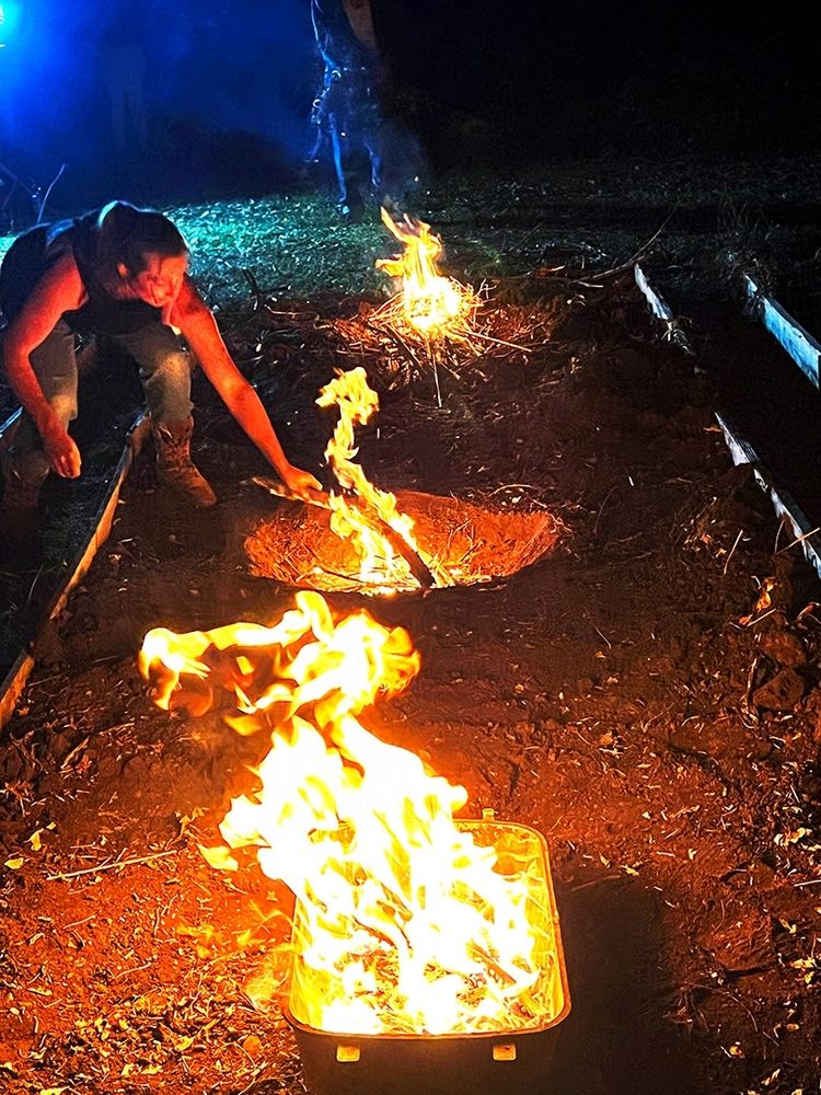 Photo of a woman feeding one of 3 roaring fires in pits