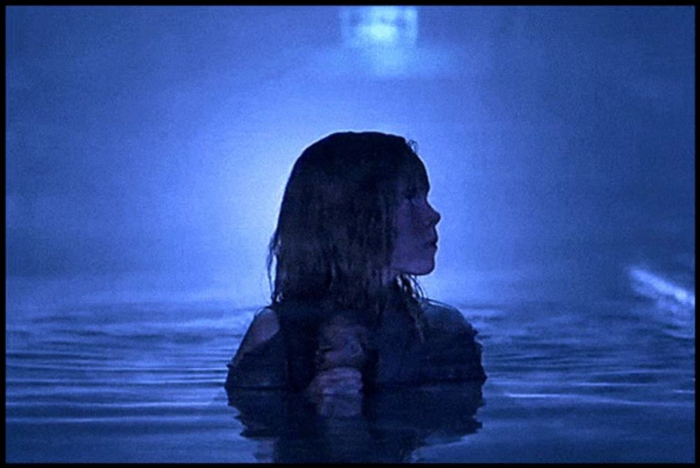 a woman standing in a body of water with a ghost in the background