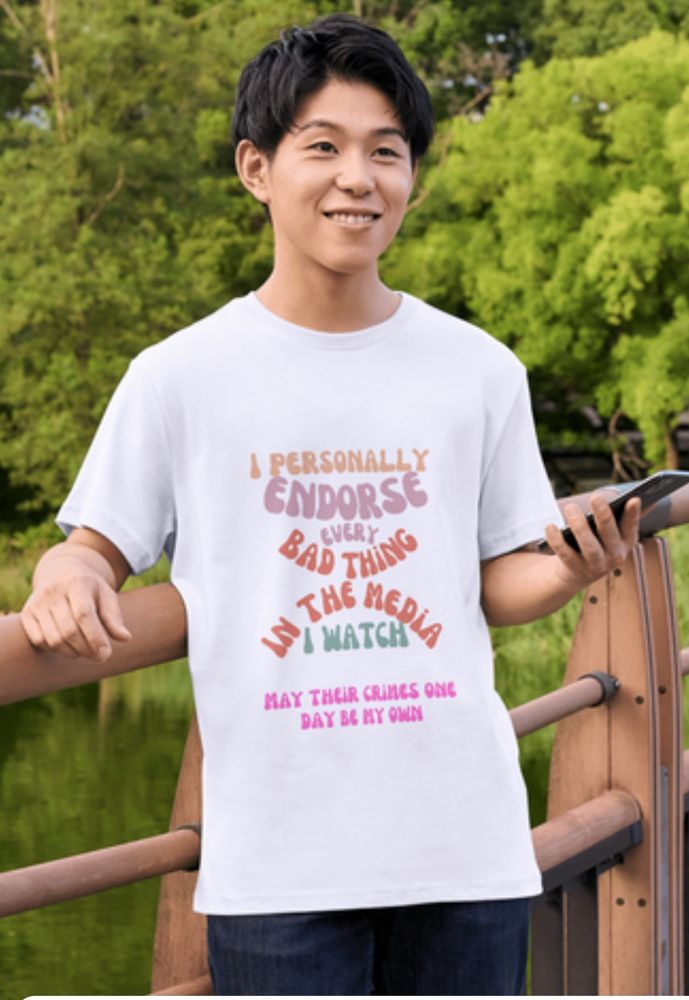 A stock photo of a man holding a phone wearing a shirt that says “I PERSONALLY ENDORSE EVERY BAD THING IN THE MEDIA I WATCH. MAY THEIR CRIMES ONE DAY BE MY OWN”