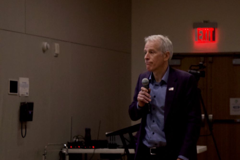Hedge fund manager Whitney Tilson pictured looking defeated while holding a microphone and looking off in the distance