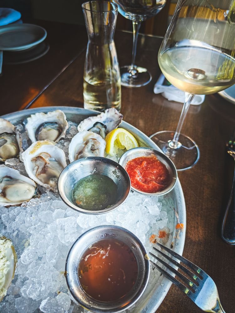 A dozen happy hour oysters on ice, with accoutrements. Off to the side is a crisp glass of white wine.