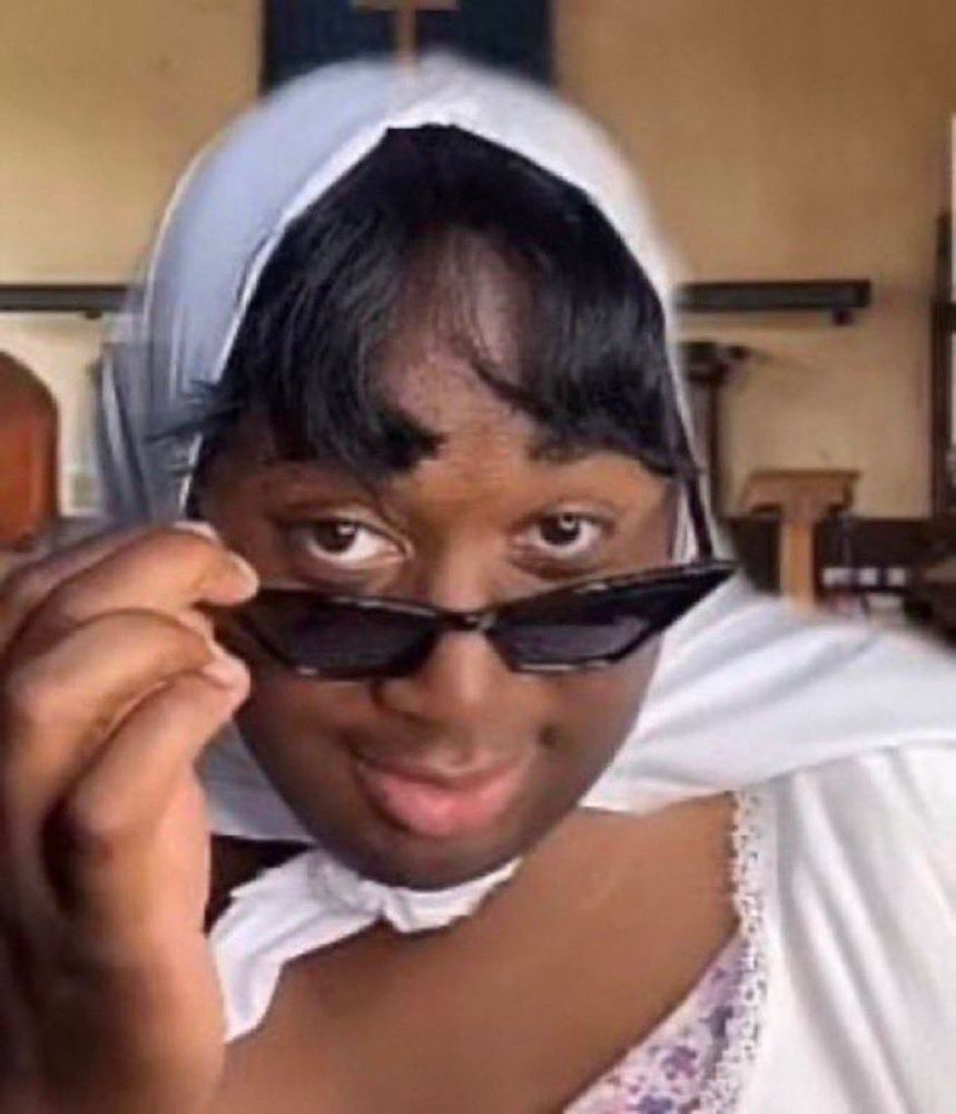 A woman with a white headscarf is taking off her sunglasses with an inquisitive look on her face