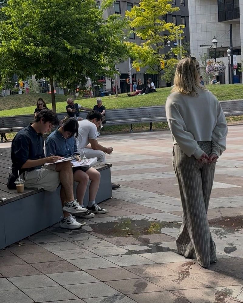 Flo stands next to a couple sitting down in an urban park, filling in a survey