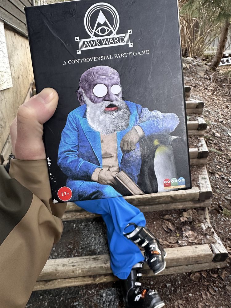 Image shows the Awkward card game box with legs matching Wicks coming out from the bottom but wearing ski boots