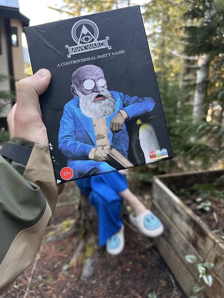 Image shows the Awkward card game box with legs matching Wicks coming out from the bottom but wearing slippers