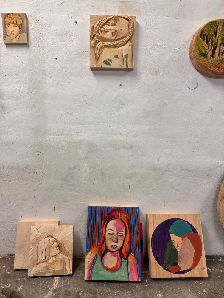 Eine Wand, an der Portrait Holzreliefs hängen und lehnen.