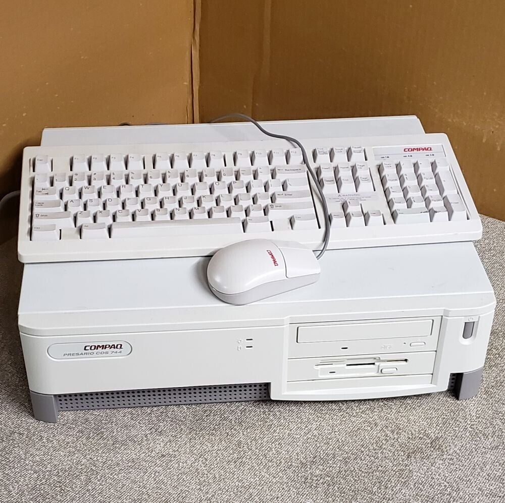 a compaq presario cds 744 horizontal desktop with its win keyless keyboard and wired ball mouse sitting atop, no monitor in sight. the desktop has a cd rom drive and a floppy disk drive on the right, and some visible ventilation holes along the lower left side. its a two tone colorway, with the lower half being a light gray and the upper being a yellowing not quite beige white. not my photo but one I found online.
