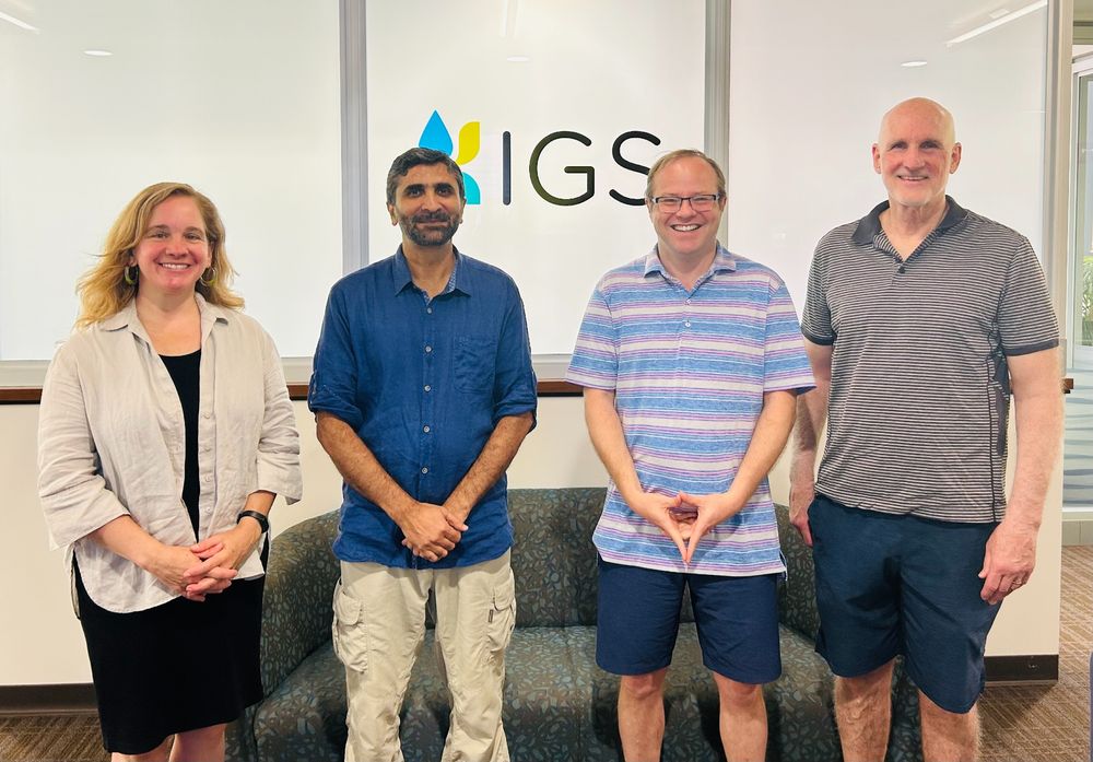 Four scholars in front of the IGS logo sign in an office.