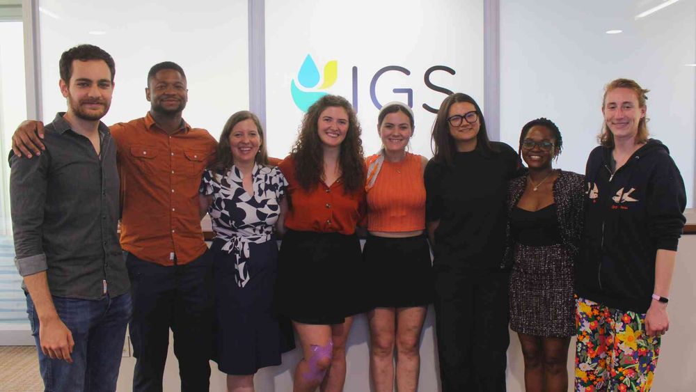 A group of eight smiling students in front of the IGS logo.