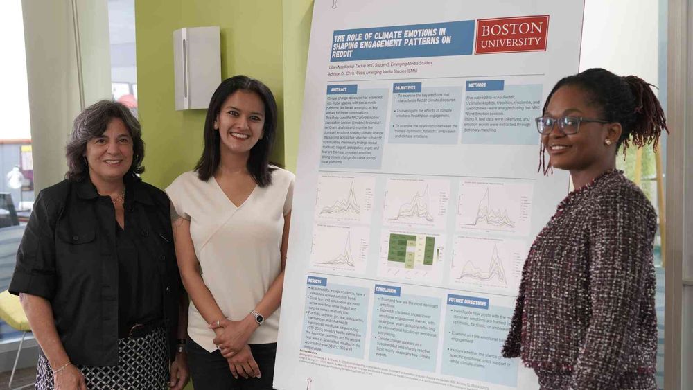 Three people smile in front of a Boston University research poster.
