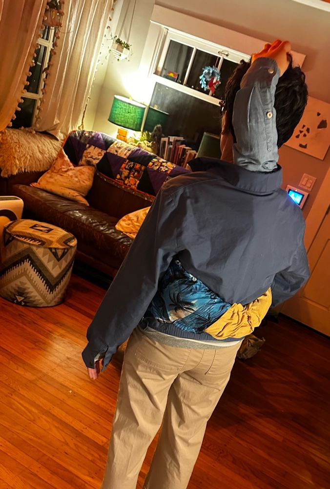 my weekend at bernie’s costume from the back- you can see a fake arm wearing a hawaiin shirt and yellow long sleeved shirt (like larry’s) around my waist. there is a fake arm wearing a blue button down (like richards) coming out of the back of my jacket and the hand is on top of my head. 