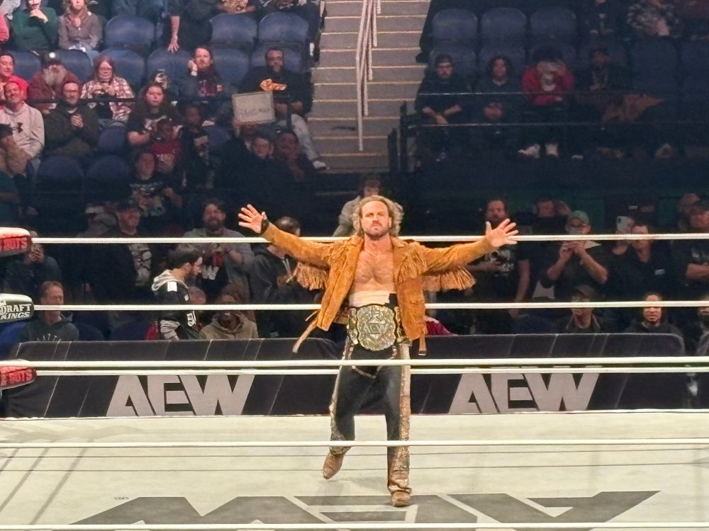 Hangman Adam Page of AEW posing with his Men’s World Championship belt before a match while standing in the middle of a wrestling ring 