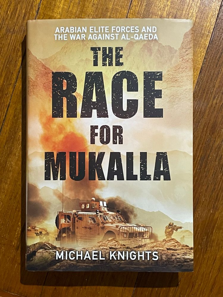 The cover of the book “The Race for Mukalla” by Michael Knights. The cover features an Oshkosh MRAP armoured vehicle in a mountainous desert landscape.