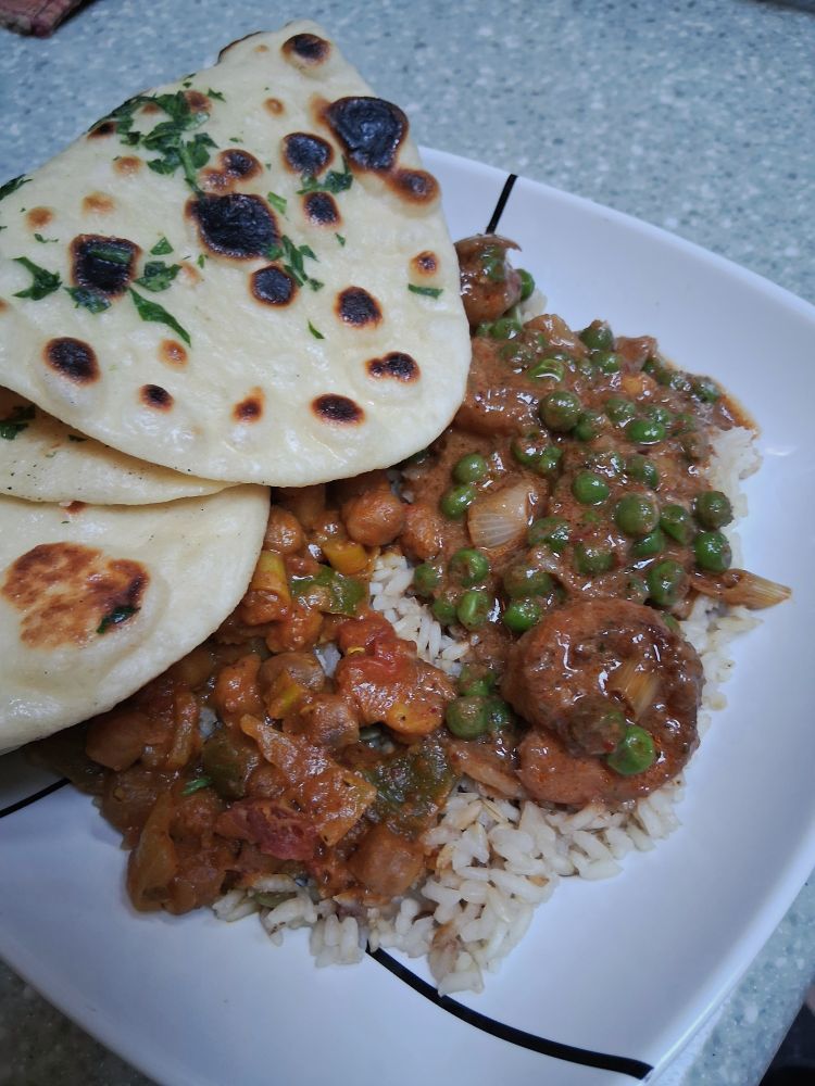 Bowl of red curry with peas and shrimp over rice, with 2 flatbreads.