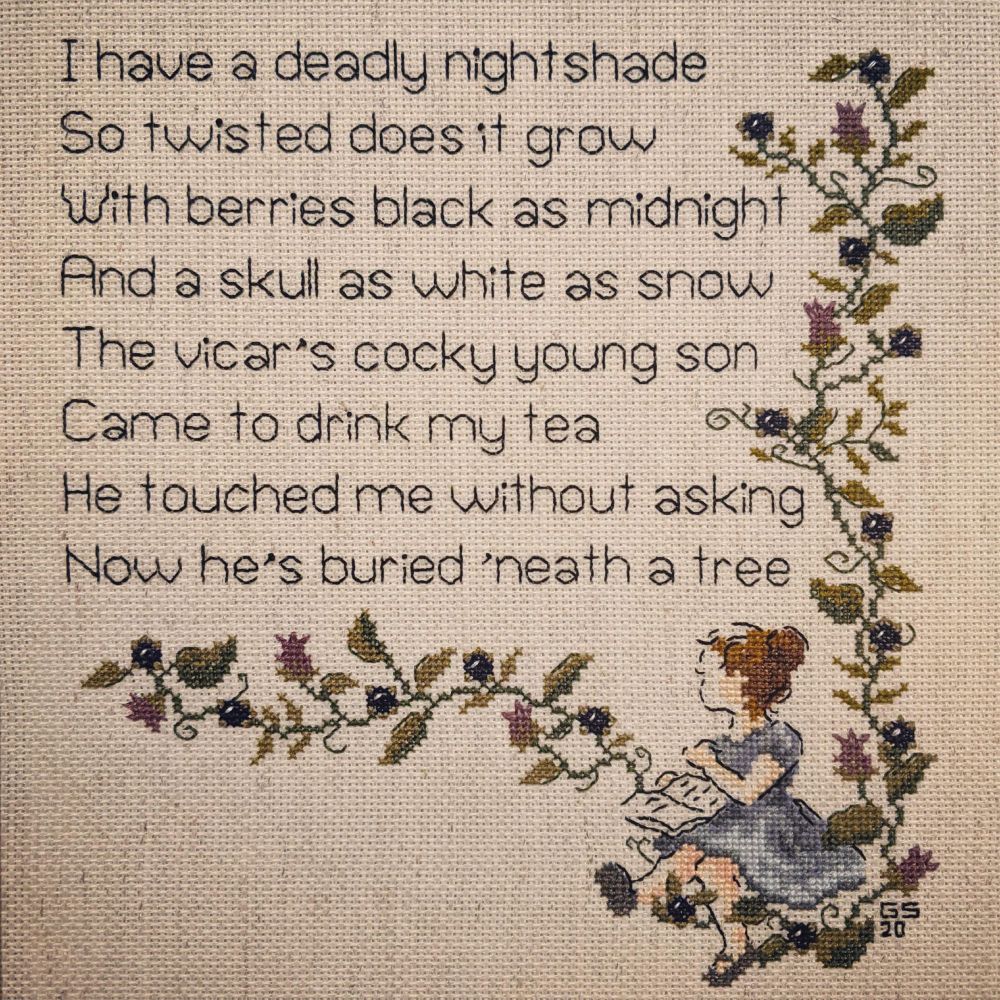 Counted cross-stitch with a white girl in a blue dress with brunette hair sitting among nightshade berries and vines

The poem reads: 
I have a deadly night shade
So twisted does it grow
With berries black as midnight
And a skull as white as snow
The vicar's cocky young son
Came to drink my tea
He touched me without asking
Now he's buried 'neath a tree