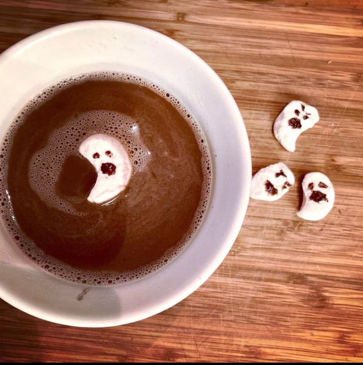 Hand cut ghost shape marshmallows with silly chocolate syrup faces. One is floating in hot chocolate. 