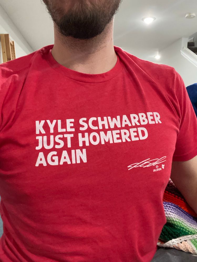 A bearded man shows off his “KYLE SCHWARBER JUST HOMERED AGAIN” shirt, again