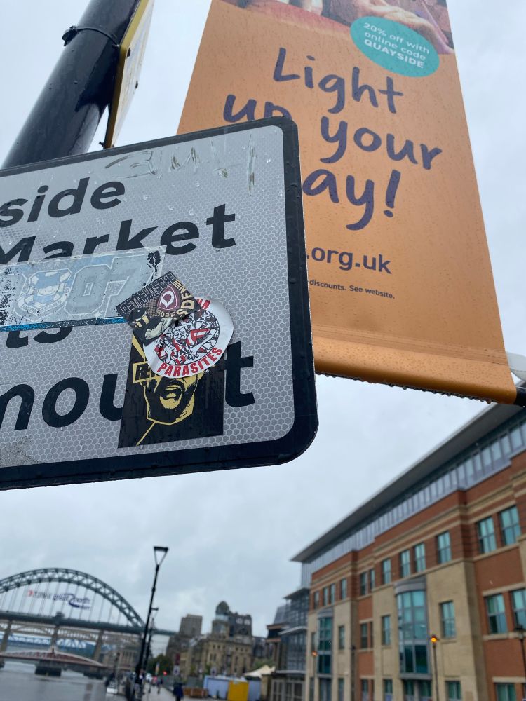 A Dynamo Dresden sticker on a sign in Newcastle with the Tyne Bridge in the background on a rainy day. 