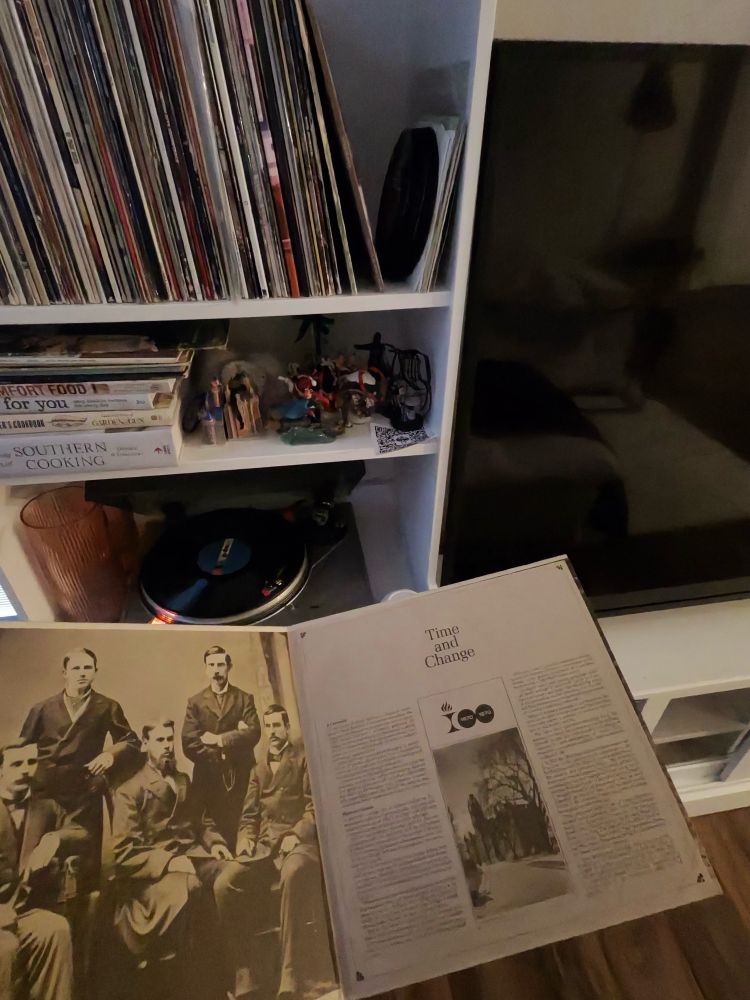 The first page of the record with the gate folds showing an old 1800s picture of men who are the first graduating class of Ohio Ohio State University. In the background, there’s a record player with books ornaments, a TV and more records.