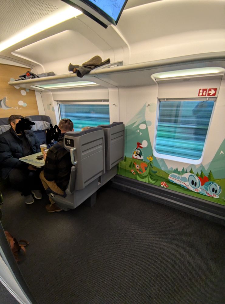 Blick auf die linke Seite des Kleinkindabteils. Rechts ist Platz für Kinderwägen, links sind vier Sitzplätze um einen Tisch herum.