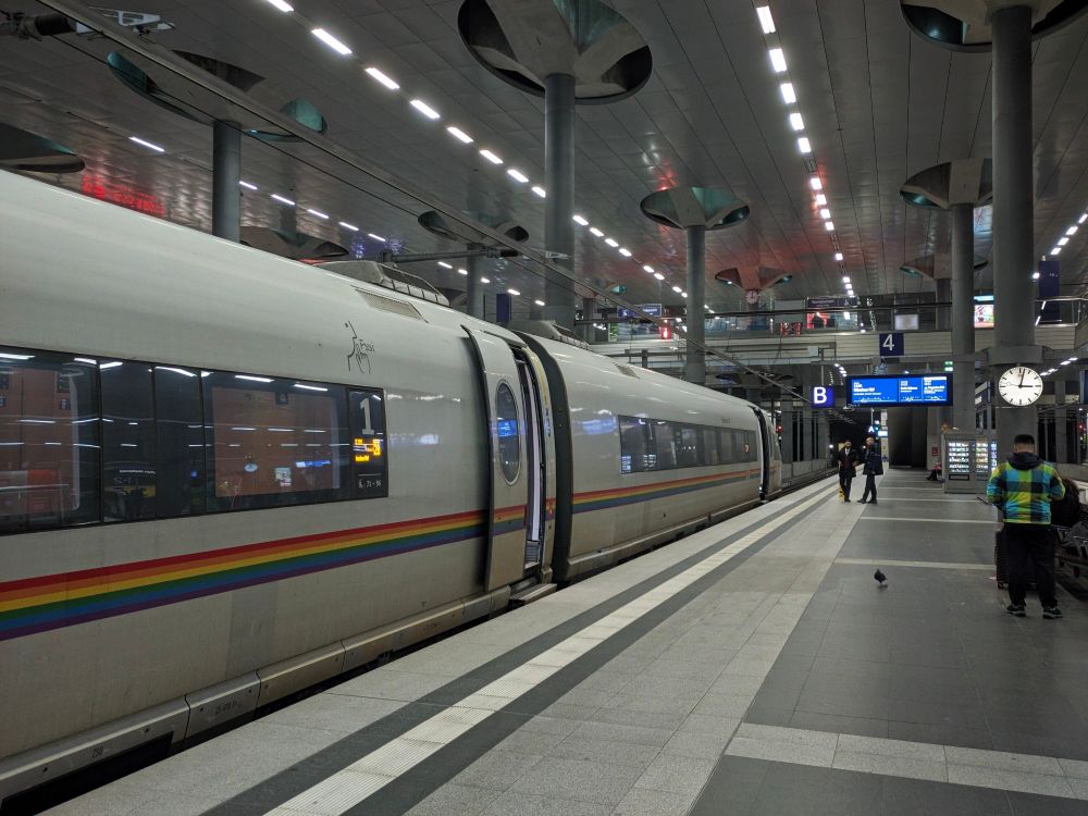Ein ICE 3 am Bahnsteig im Untergeschoss des Berliner Hauptbahnhofs. Der Zierstreifen des ICE ist ein Regenbogen.