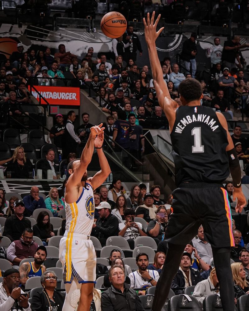 atleta victor wembanyama (de uniforme preto) tentando contestar o arremesso do atleta stephen curry (de uniforme branco) durante o jogo san antonio spurs x golden state warriors. 