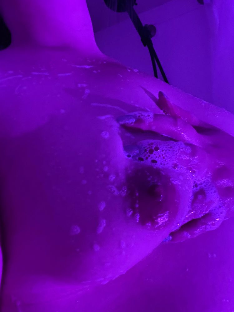 A woman squeezes her bare, soap covered breast. 