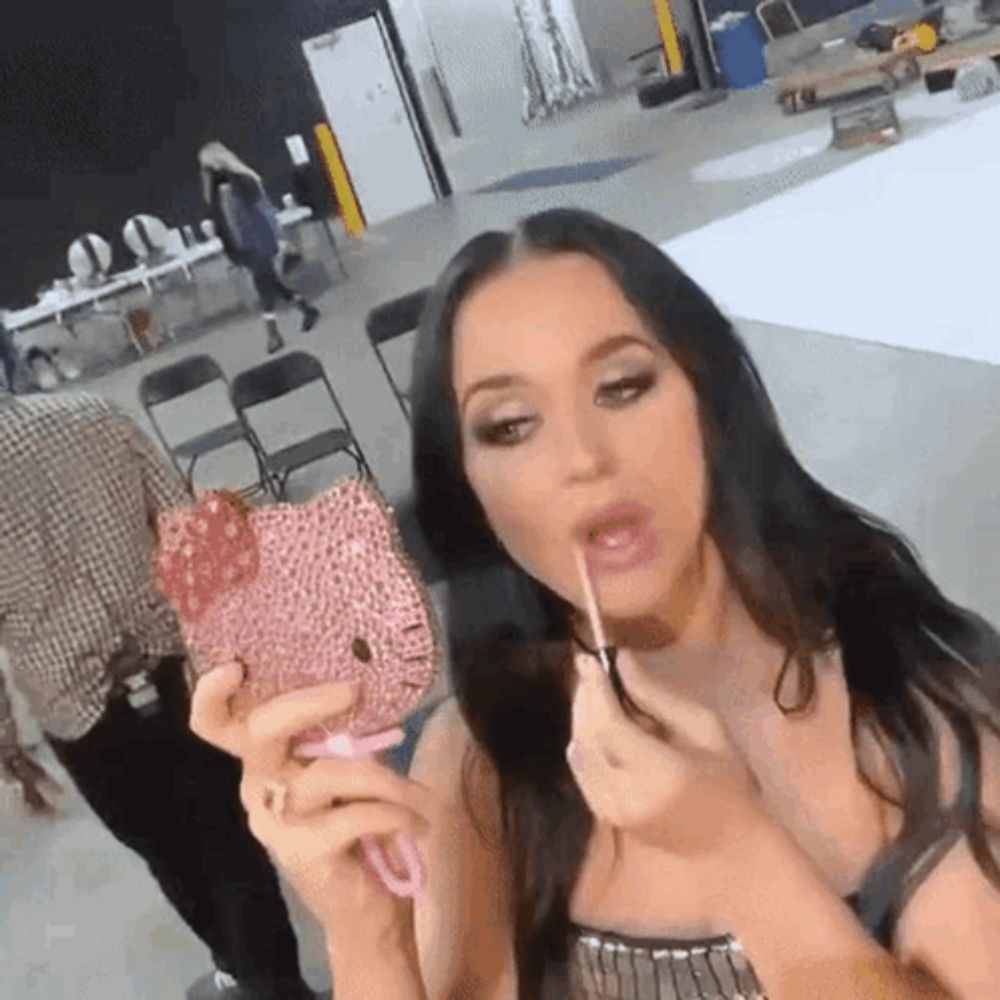 a woman is applying lipstick in a room while holding a mirror .