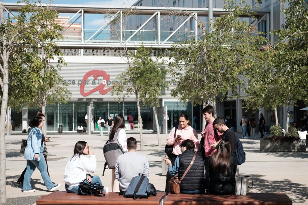 Estudiants de la Universitat Rovira i Virgili asseguts a un banc a la plaça de la Concòrdia, davant del CRAI del campus Catalunya.