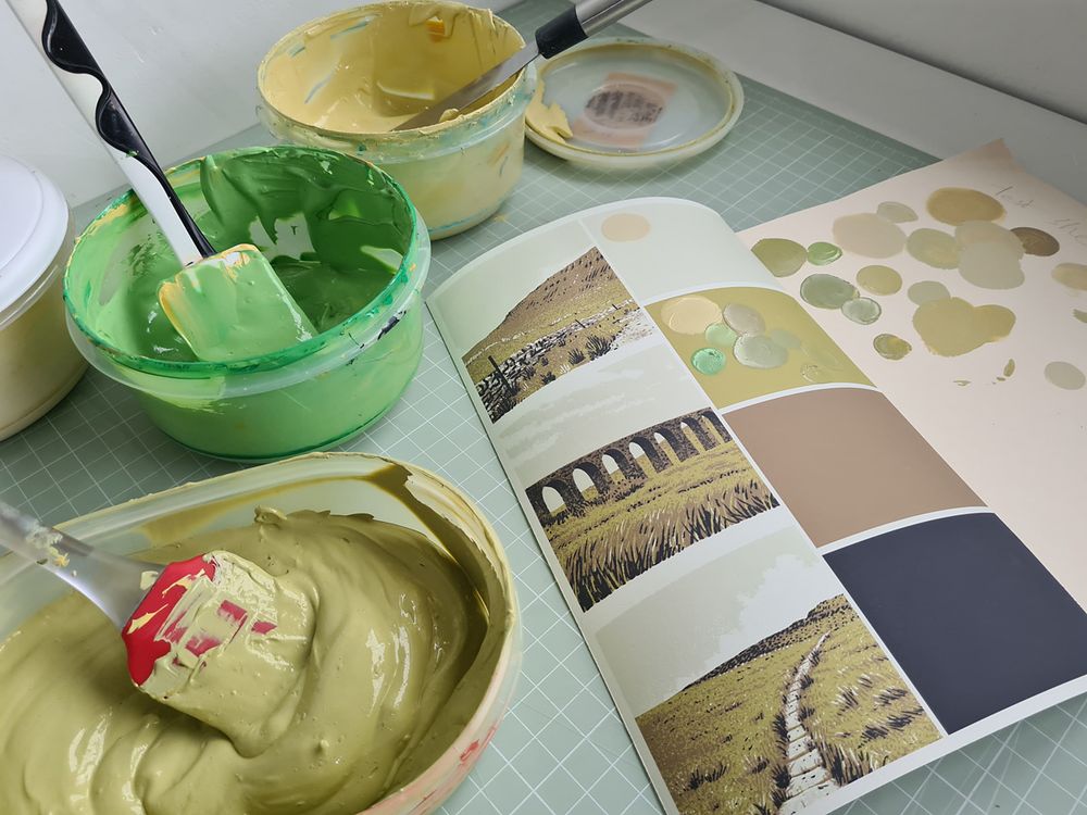 Different pots of green ink being mixed and colour matched ready for screenprinting a poster of the Yorkshire Three Peaks on the desk of artist and print maker Graham Pilling, Army of Cats Creative Studio.