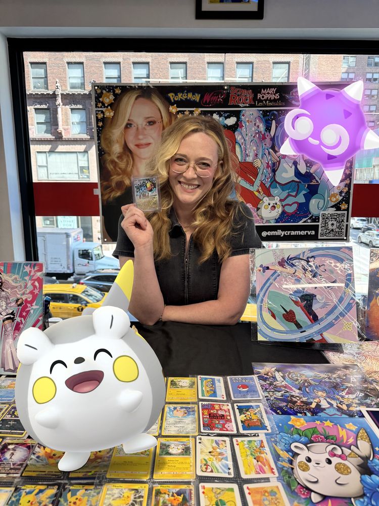 Emily Cramer holding a signed Farigiraf card behind her desk at Nxt Legaci in NYC. She is joined by Minior and Togedemaru, both of which she has voiced in the English dub of the anime (Pokémon GO #GOSnapshot)
