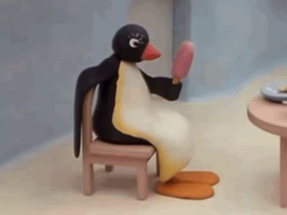 a penguin is sitting in a chair holding an ice cream cone and looking at itself in the mirror .