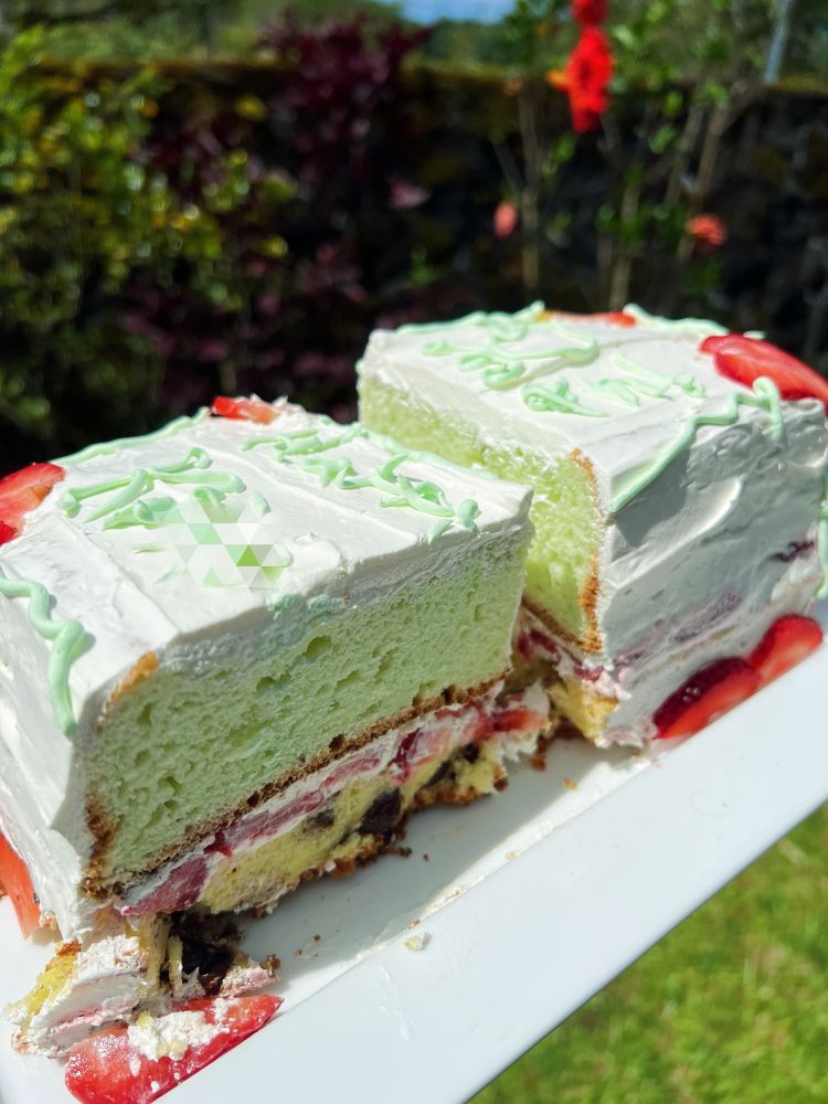 A white frosted, strawberry-covered two-layer birthday cake with a light green top layer made out of pistachio and a yellow bottom layer made out of vanilla and chocolate chips. Yum!