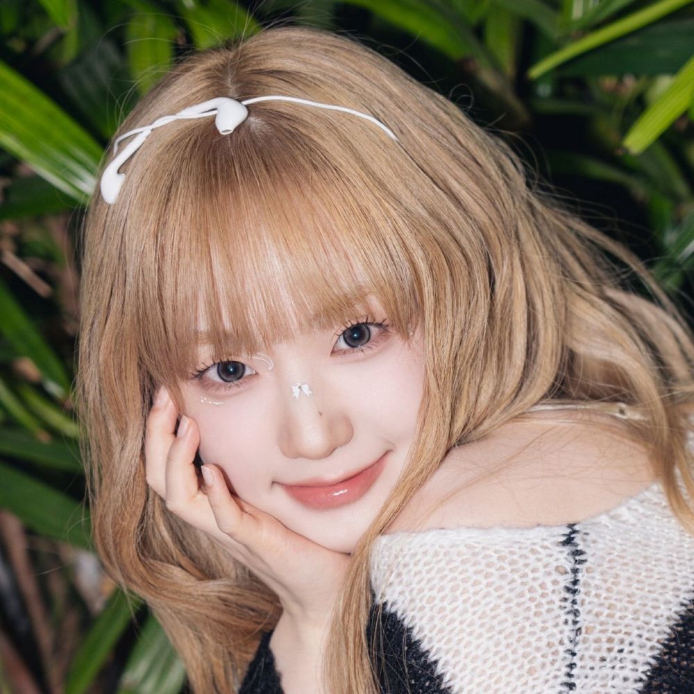 Seoyeon from tripleS with earbud cords tied like a headband. There are some white and sparkly stickers around her left eye and a little bow on the bridge of her nose.