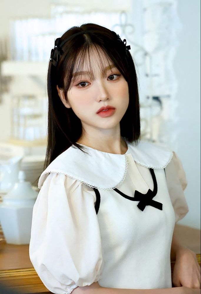Gowon with black hair wearing a white outfit with puffy sleeves and a cute collar, looking very poised.