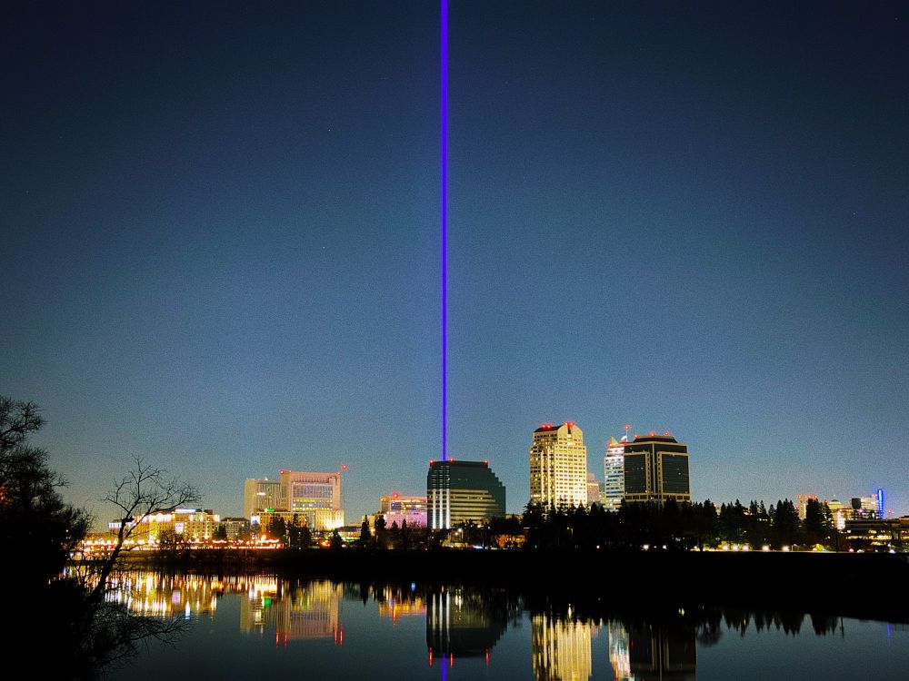 Purple laser beam emanates into the night sky, surrounded by buildings