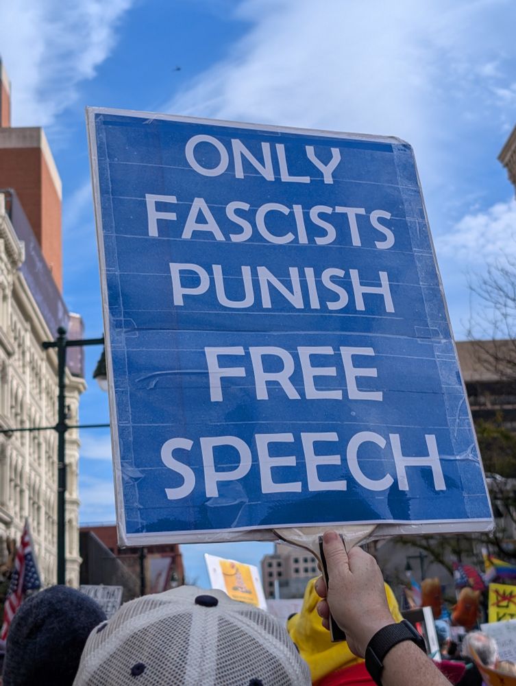 Someone holding up a sign that says, "Only fascists punish free speech" among a crowd marching in protest. 