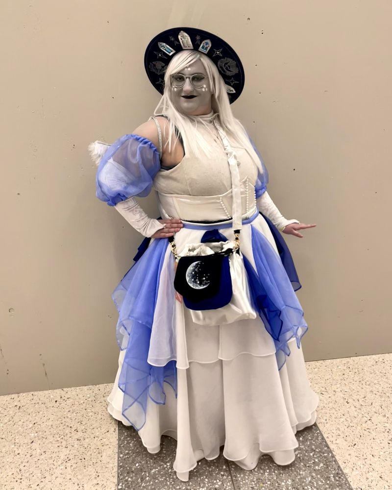 Personal project, worn for Twin Cities Con 2024; cosplay of Emily from Hazbin Hotel

Items made from scratch:
- white velvet sleeveless turtleneck
- white velvet gauntlet gloves
Periwinkle organza puff sleeves
- white satin corset belt with pearl beading
- black stiff-tulle petticoat; worn underneath for volume
- white floor-length circle skirt; made using thrifted tablecloths and sheer curtain fabric
- sheer midi overskirt with periwinkle organza godets and navy blue layered overlays
- white satin decorative cover for crossbody bag