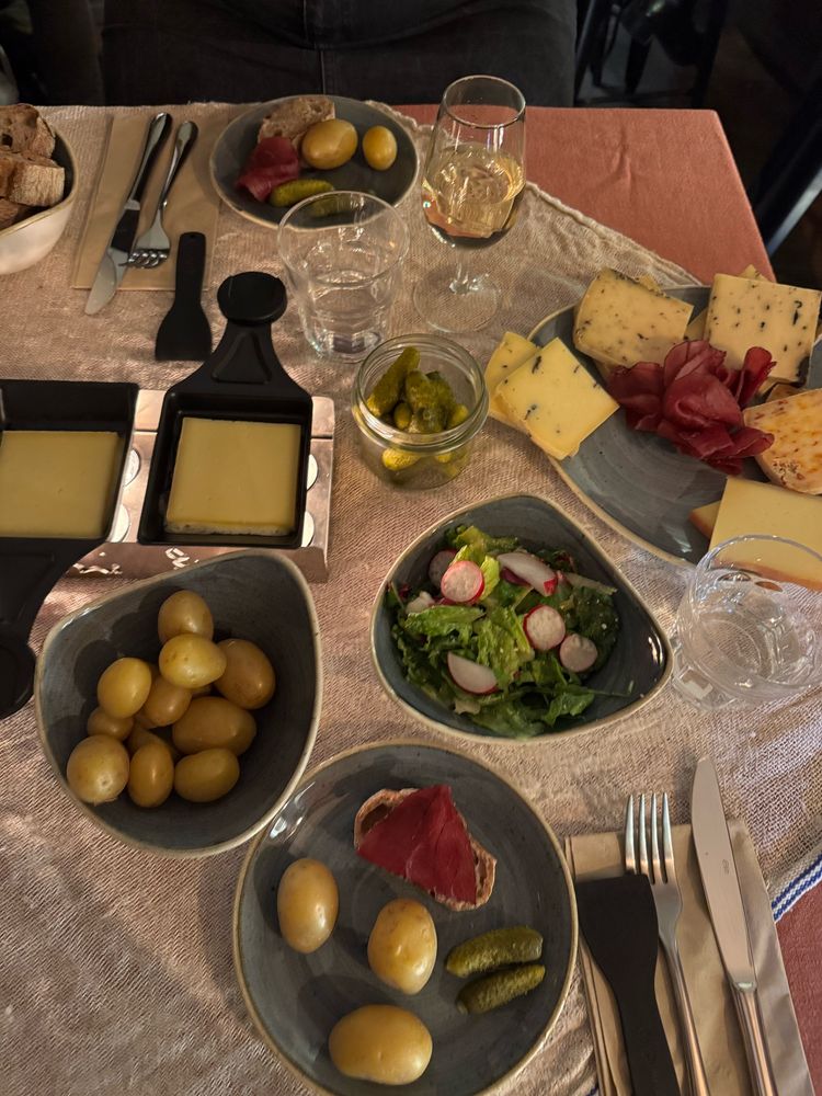 Raclette cheese, bowl of boiled potatoes, salad, pieces of baguette, some cornichons and some cured meat