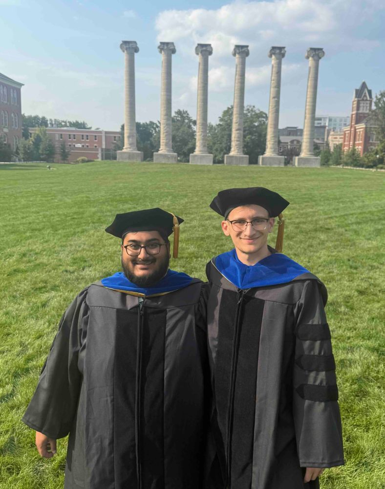 Michael Pisias and Shawn Thomas standing in regalia at columns at University of Missouri-Columbia
