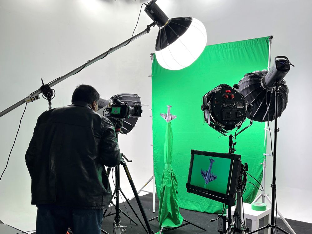 Person operating professional camera equipment in a studio with a green screen and various lighting rigs.
