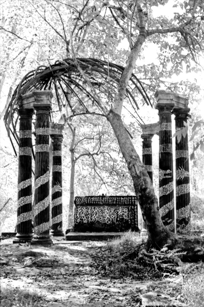 Alter in ruins with a tree falling, knocking off the roof. Black and white graffiti covers the entire structure