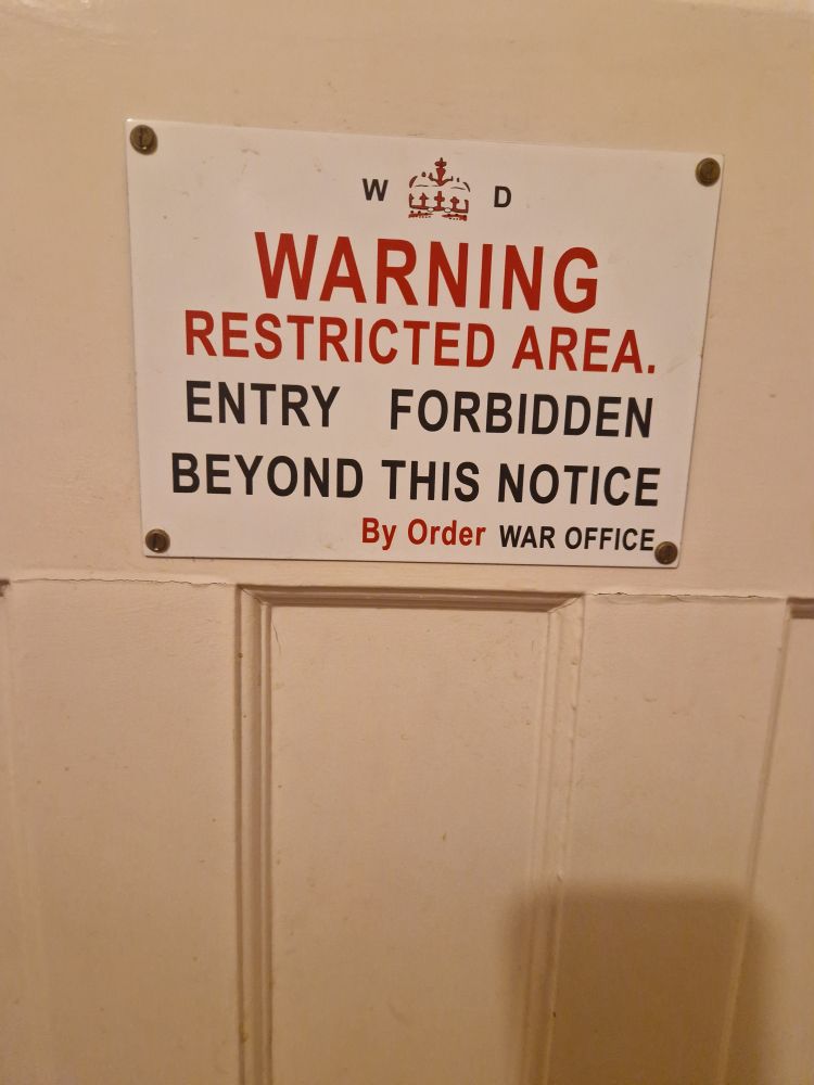 WWII-era enamel sign saying "Warning. Restricted Area. Entry forbidden beyond this notice. By Order War Office" on a toilet door.